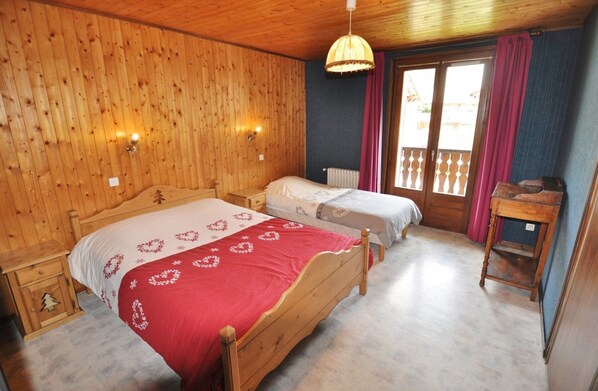 A wooden-paneled room with two beds, a wooden nightstand, a small table, and a window with curtains.