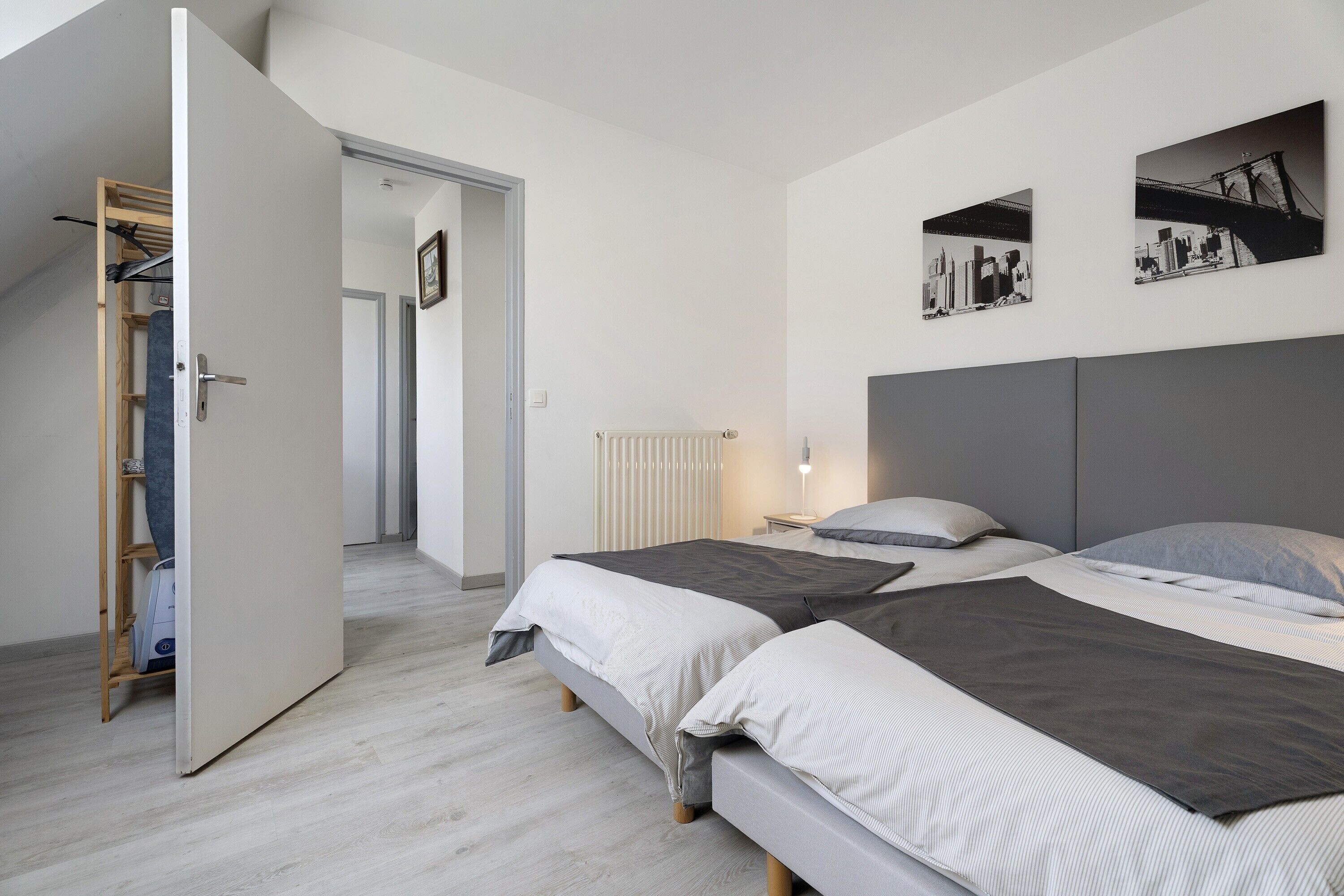 Une chambre moderne avec deux lits, un dressing et une œuvre d’art représentant un paysage urbain accrochée au mur.
