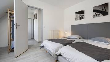 Une chambre moderne avec deux lits, un dressing et une œuvre d’art représentant un paysage urbain accrochée au mur.