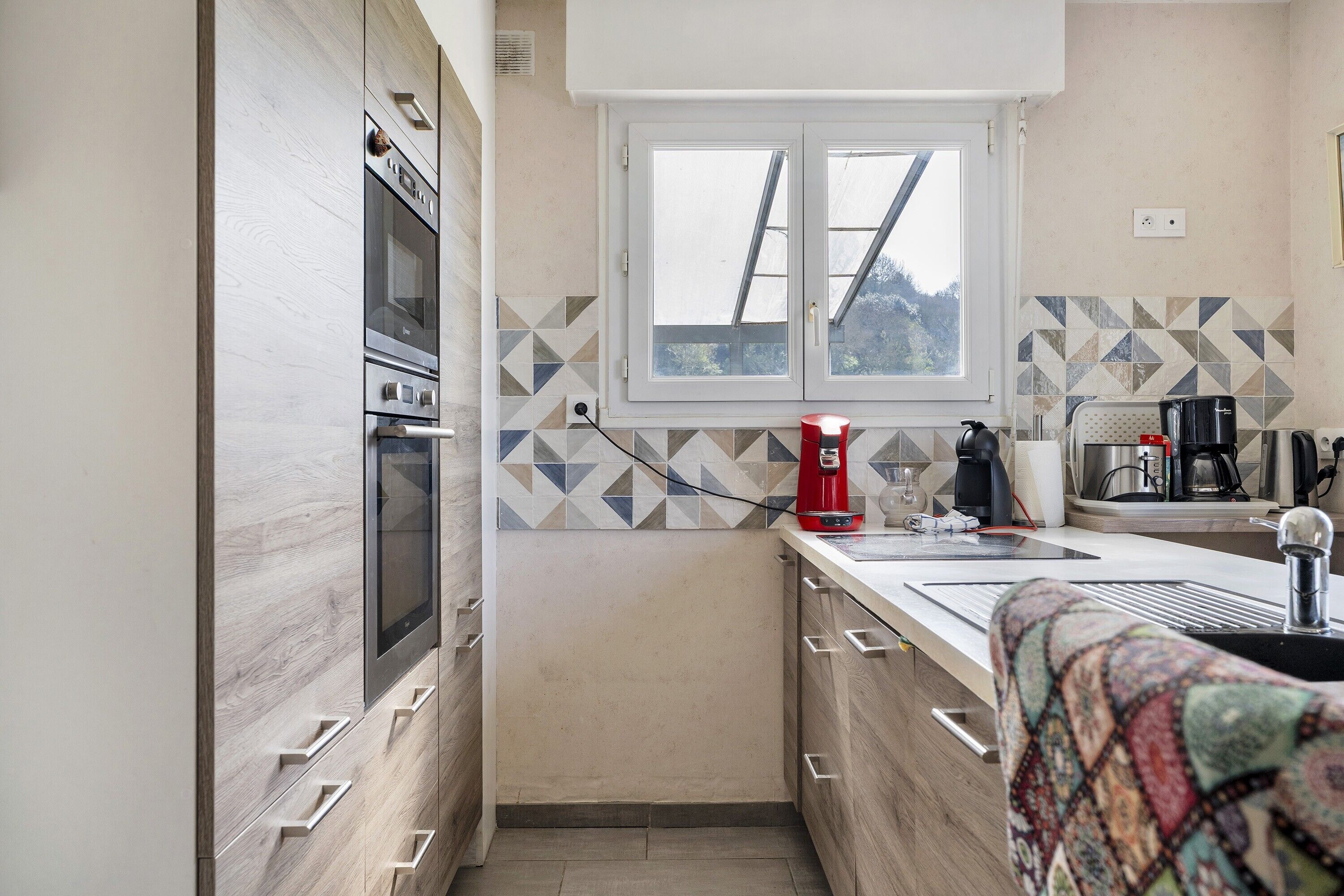 Una cocina compacta con horno integrado, ventana con vistas y un salpicadero decorado.