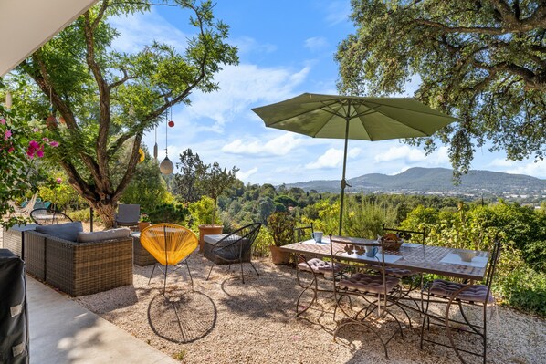 Une terrasse extérieure aménagée avec des meubles en osier, une table et des chaises, offrant une vue sur un paysage pittoresque.