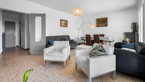 Een moderne woonkamer met een bank, fauteuils, een eettafel en een keukenhoek.