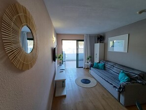 A modern living room with a sofa, a TV, a mirror, and a view through a glass door. - Holiday Apartment 'Amazing' with Sea View, Shared Pool and Wi-Fi (Mogán)