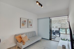 A modern living room with a grey sofa, two framed artworks, a sliding glass door leading to an outdoor seating area.