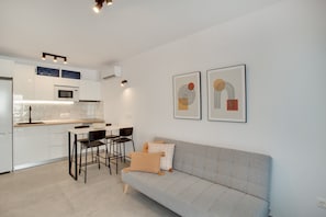 A modern kitchen with white cabinets, a microwave, and a dining area with a grey sofa and two chairs.