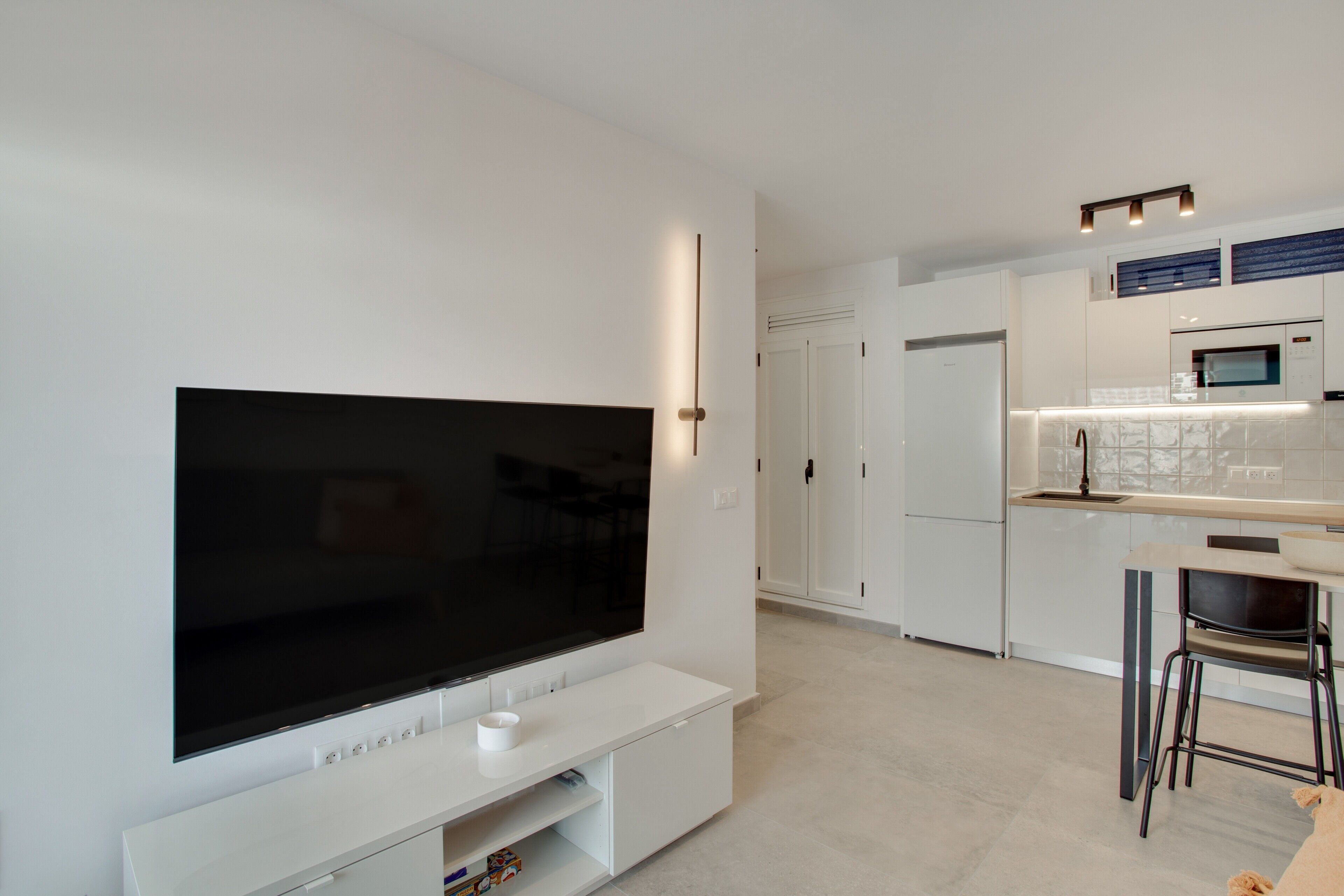 Een moderne keuken met een flatscreen televisie, witte kasten en een gezellig eethoekje.