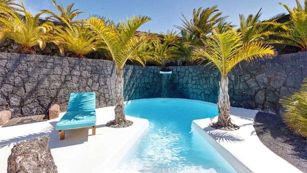 A swimming pool with a stone wall, palm trees, and a lounge chair. - 'Villa La Cueva' with Shared Pool, Private Terrace and Wi-Fi (Teguise)