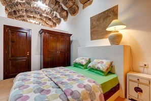 Une chambre à coucher avec un lit, une literie verte, une lampe, une table de chevet et une lampe fixée au mur.