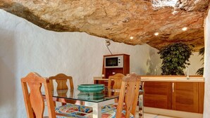 A rustic dining area with a glass table, wooden chairs, a TV on a wooden cabinet, and a plant in the background. - Vacation Villa 'El Cactus' with Shared Pool and Wi-Fi (Teguise)