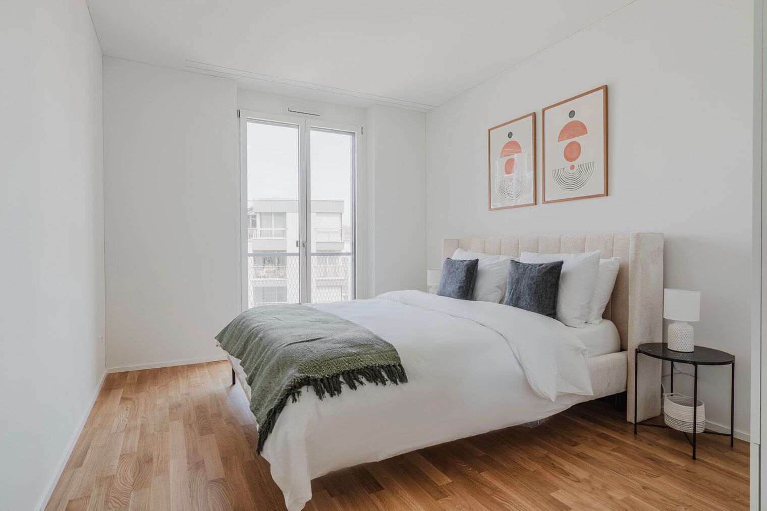A bedroom with a bed, a nightstand, a lamp, and two framed artworks on the wall.