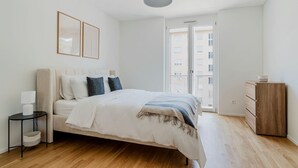 A modern bedroom with a bed, bedside table, lamp, and a dresser.