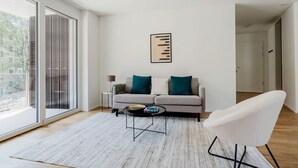A modern living room with a sofa, a coffee table, and a chair. There is a large window with a view of the outside.