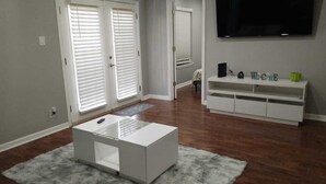 Una sala de estar con un mueble blanco para el equipo multimedia, un televisor de pantalla plana y una mesa de centro blanca.
