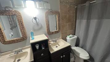 Un baño con lavamanos, espejo, inodoro y cortina de ducha.