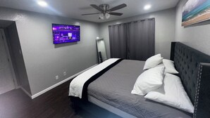 Un dormitorio con cama, ventilador de techo, televisor en la pared y un cuadro.