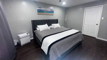 A bedroom with a bed, a nightstand, a ceiling fan, a door, and a painting on the wall.