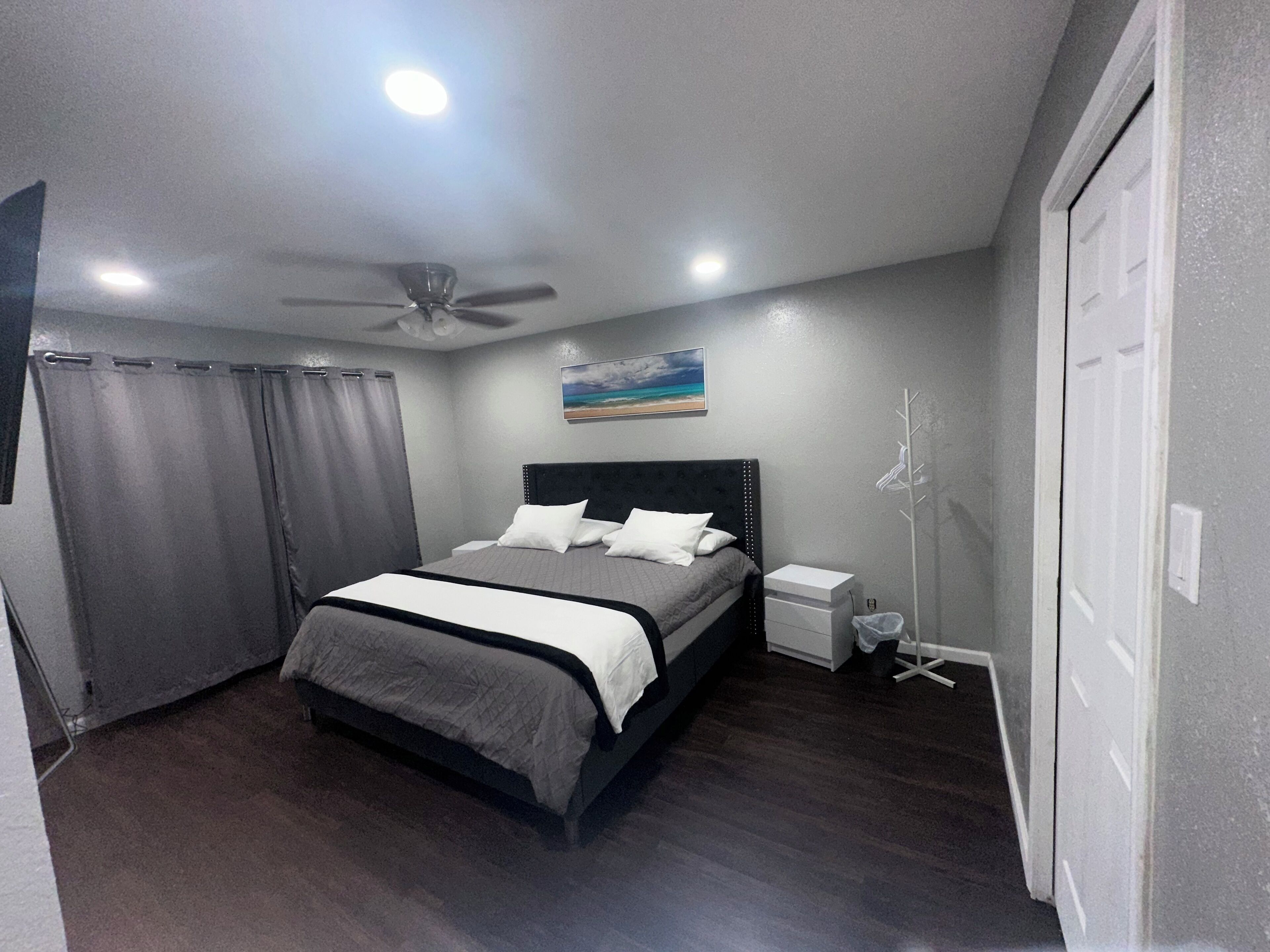 Een slaapkamer met een bed, een plafondventilator, een nachtkastje en een aan de muur bevestigd schilderij.