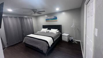 Een slaapkamer met een bed, een plafondventilator, een nachtkastje en een aan de muur bevestigd schilderij.