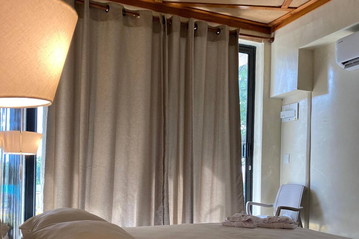 Um quarto espaçoso com uma cama grande, uma cadeira e um abajur.