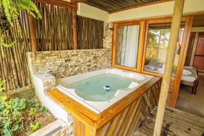 A wooden hot tub with a stone wall backdrop, a wooden deck, and a glass door leading to an outdoor area. - Ada Marina (Turbaco)