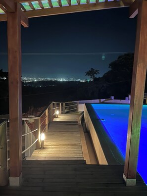 A wooden deck leading to a swimming pool with a cityscape view at night. - Ada Marina (Turbaco)