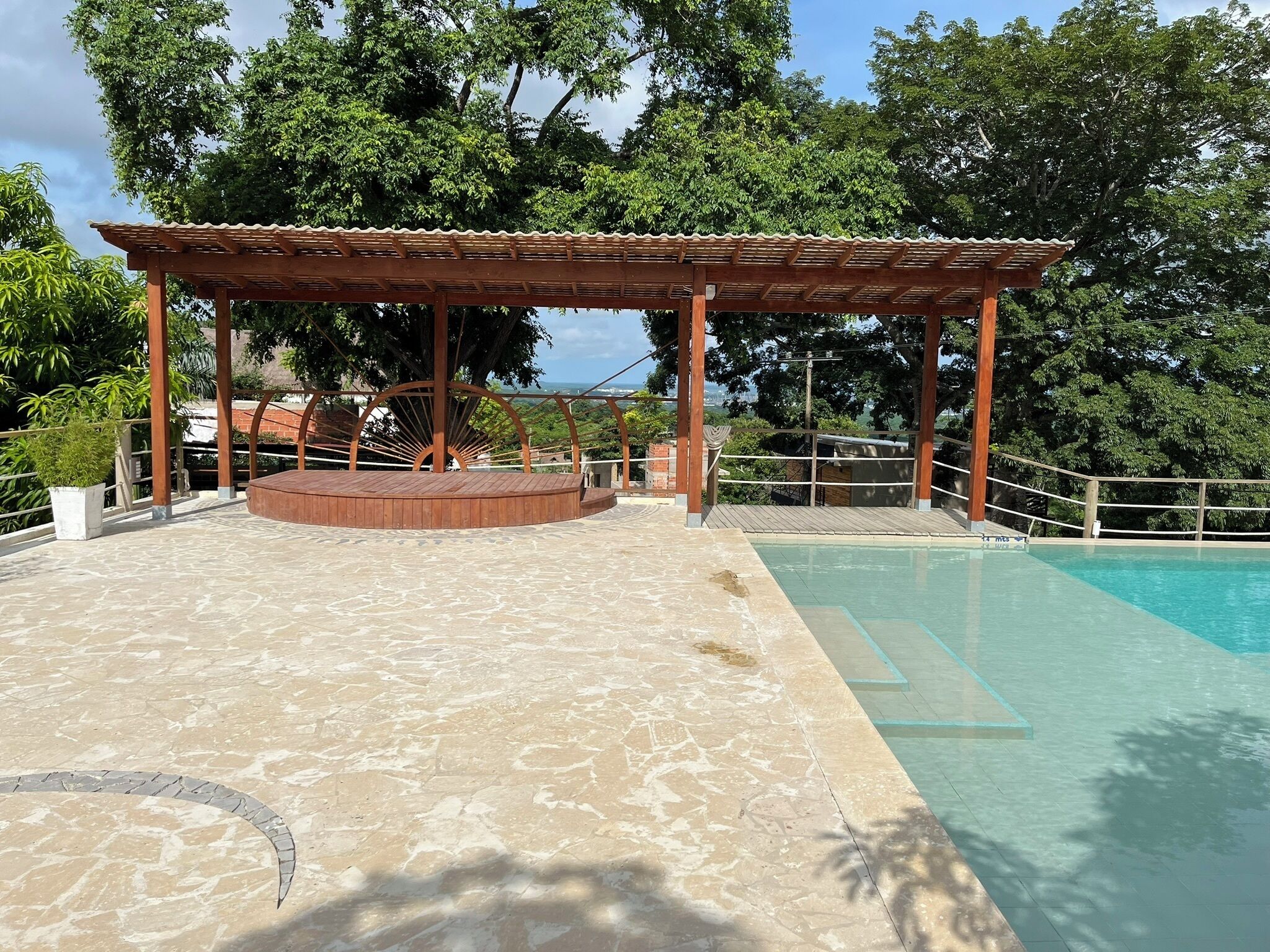 Un área junto a la piscina con una pérgola de madera, un espacio de estar circular y vista despejada al océano.