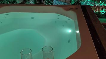 Un jacuzzi con dos copas de vino sobre una mesa, con vistas a un paisaje urbano nocturno.
