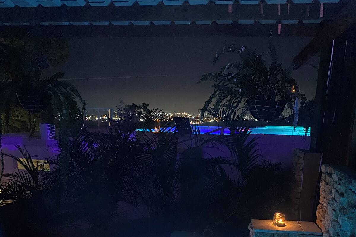 Uma banheira de hidromassagem com duas velas acesas, cercada por paredes de pedra e vista para a cidade à noite.