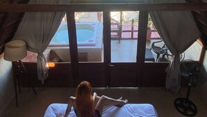 Ein Zimmer mit hoher, geneigter Decke und einem großen, dreieckigen Fenster. Ein Bett steht unter dem Fenster, und auf dem Boden befinden sich ein Ventilator und eine Lampe.
