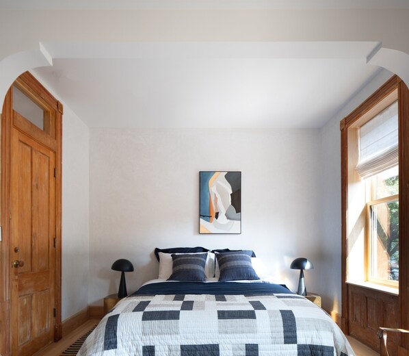 A bedroom with a bed, two bedside tables, a painting on the wall, and wooden doors.