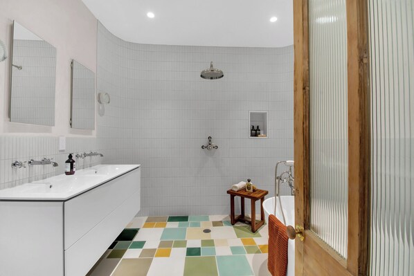 A modern bathroom with a white tiled shower, a sink with a mirror, and a small wooden stool.