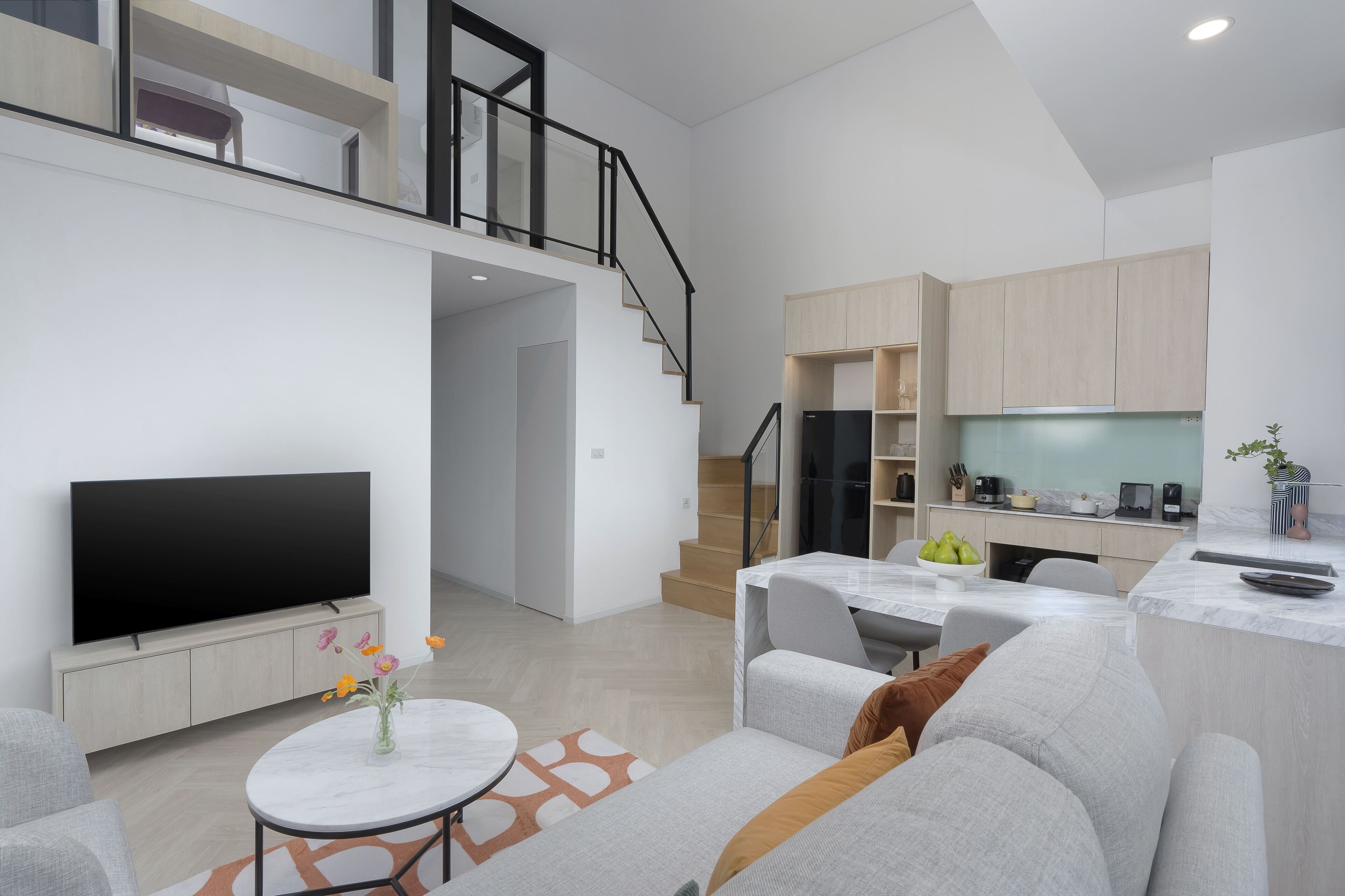A modern apartment with a living room, dining area, kitchen, and a staircase to an upper level.