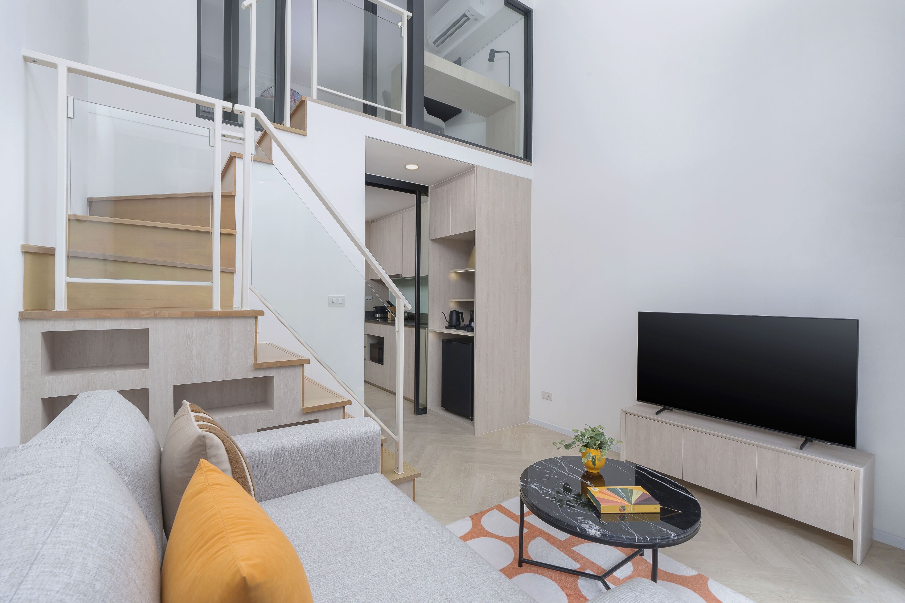 A modern living room with a staircase, a flat-screen TV, a sofa, and a coffee table.