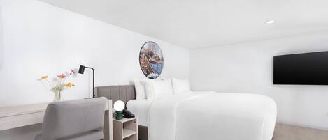 A modern hotel room with a bed, desk, chair, and a wall-mounted TV.