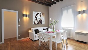 A modern living room with a white sofa, a dining table with chairs, a painting on the wall, and a radiator. - Dimora San Zanipolo by Wonderful Italy (Venice)