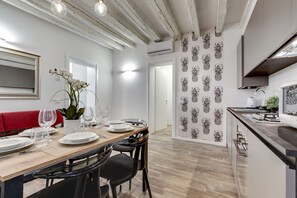 A modern dining area with a wooden table set for four, black chairs, a red bench, and white walls with pineapple wallpaper.