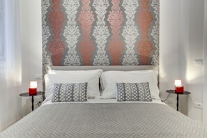 A neatly made bed with a patterned bedspread, two pillows, and two bedside tables with red lamps.