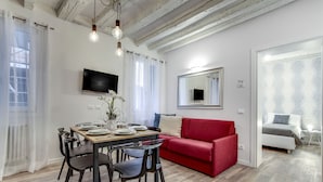 Een moderne woonkamer met een eethoek, een rode bank, een aan de muur bevestigde televisie en een grote spiegel.