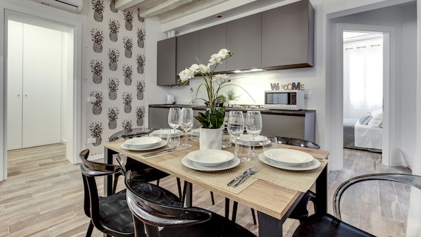 Een moderne eethoek met een houten tafel voor vier personen, omringd door zwarte stoelen. Op de tafel staat een witte vaas met bloemen, en er staan wijnglazen en borden klaar voor een maaltijd.