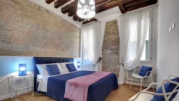 A bedroom with a large bed, a wooden floor, a brick wall, and a chandelier. - San Marco Promenade by Wonderful Italy (Venice)