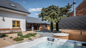 A hot tub in a backyard with a wooden deck, a bench, and a house with a sloped roof.
