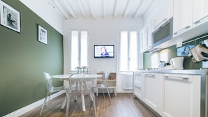 A modern kitchen with white cabinets, a dining area with clear chairs, and a television mounted on the wall. - Ca d Oro Cozy Suite by Wonderful Italy (Venice)
