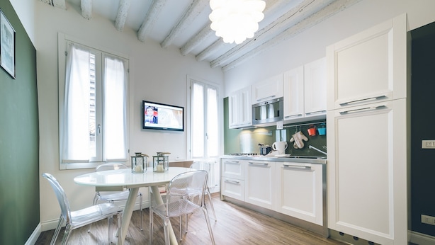 A modern kitchen with white cabinets, a dining table with chairs, and a television mounted on the wall. - Ca d Oro Cozy Suite by Wonderful Italy (Venice)