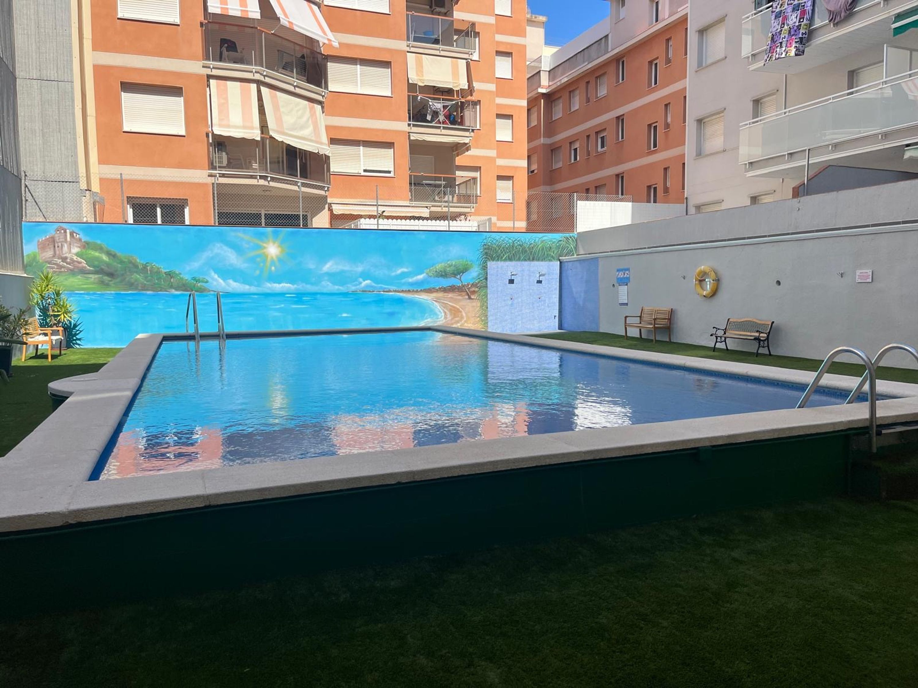 A swimming pool with a mural of a beach scene, surrounded by apartment buildings.