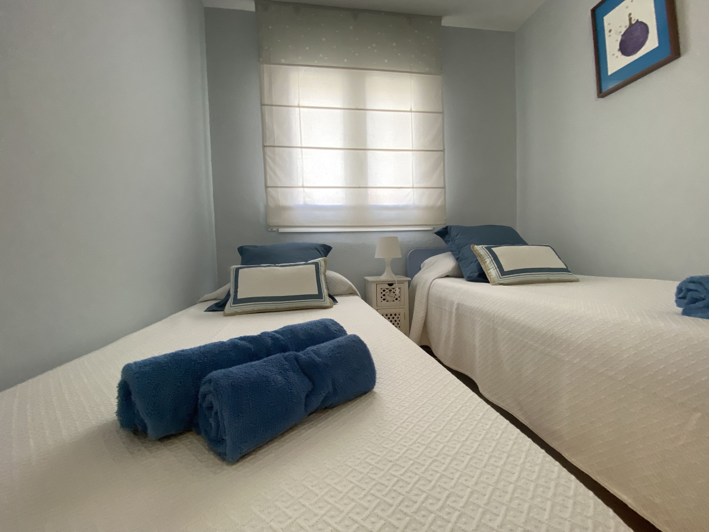 A bedroom with two beds, each with a pillow and a rolled towel.