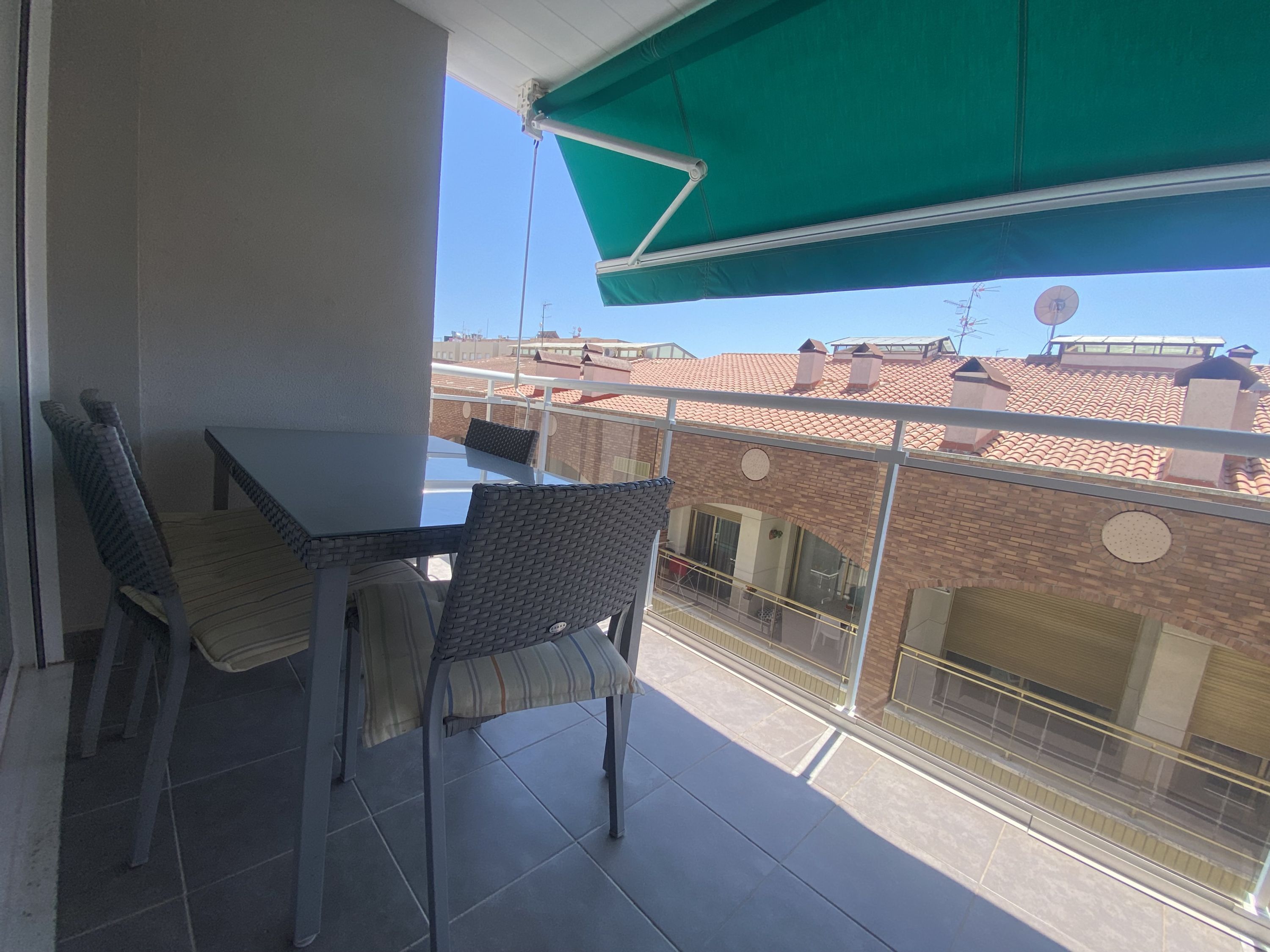 A balcony with a table and chairs, a green awning, and a view of neighboring buildings.