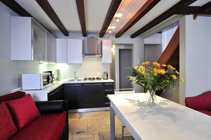 Une cuisine compacte avec des meubles blancs, un four à micro-ondes et une cuisinière. On y trouve une table à manger agrémentée d’un vase de fleurs.