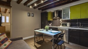A modern kitchen with green cabinets, a stainless steel range hood, and a dining area with a table and chairs. - San Giacomo Apartment by Wonderful Italy (Venice)