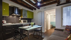 A modern kitchen with dark cabinets, a glass dining table, and a sofa in the living area. - San Giacomo Apartment by Wonderful Italy (Venice)