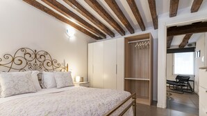 A bedroom with a bed, wooden beams, a wardrobe, and a desk with a chair. - San Giacomo Apartment by Wonderful Italy (Venice)